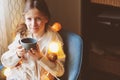 Kid girl drinking hot cocoa at home in winter weekend, sitting on cozy chair