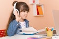 Kid girl with headphones using laptop at table in room. Online classes, teaching online. Royalty Free Stock Photo