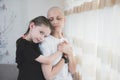 Kid girl hugs her mother with a diagnosis of leukemia near the window. Family support concept
