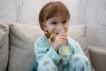 Kid girl makes inhalation with a nebulizer. sick child holding inhalator in hand and breathes through an inhaler at home