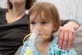 Kid girl makes inhalation with a nebulizer. sick child with mother holding inhalator in hand and breathes through an inhaler at