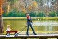 Kid girl and mother walking in lake with pull cart