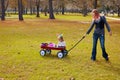 Kid girl and mother walking in park with pull cart