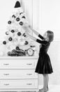 Kid girl near christmas tree waiting midnight clock. Last preparations. Child celebrate christmas at home. Favorite day