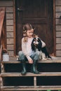 Kid girl playing with her spaniel dog, sitting on stairs at wooden log cabin