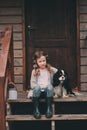 Kid girl playing with her spaniel dog, sitting on stairs at wooden log cabin Royalty Free Stock Photo