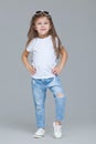 Kid girl preschooler in blue jeans, white t-shirt and sunglasses is posing isolated on grey background Royalty Free Stock Photo