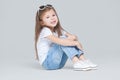 Kid girl preschooler in blue jeans, white t-shirt and sunglasses is posing sitting isolated on grey background Royalty Free Stock Photo