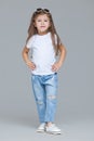 Kid girl preschooler in blue jeans, white t-shirt and sunglasses is posing isolated on grey background Royalty Free Stock Photo