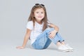 Kid girl preschooler in blue jeans, white t-shirt and sunglasses is posing sitting isolated on grey background Royalty Free Stock Photo