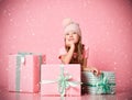 Kid girl is sitting behind gifts boxes presents guessing, dreaming of a present, waiting under the snow on pink Royalty Free Stock Photo
