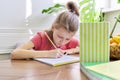 Kid girl studying at home, sitting at the desk, writing in school notebook Royalty Free Stock Photo