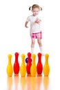 Kid girl throwing ball to knock down toy bowling pins.