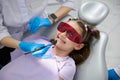 Kid girl wearing UV glasses, smiles to a doctor dentist holding dental mirror while a teeth check-up in dentistry clinic Royalty Free Stock Photo