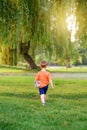 Kid going to future. Little cute toddler Caucasian boy in red t-shirt with stuffed plush toy walking alone in park with tall trees Royalty Free Stock Photo