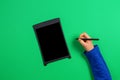 Kid hand with graphic tablet and stylus pen on green background