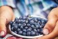 Kid hand holding bowl of freshly picked wild blueberries against bokeh green forest background Royalty Free Stock Photo