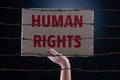 Kid hand holding cardboard paper with HUMAN RIGHTS text and rusty sharp bare wire on dark background, conceptual image Royalty Free Stock Photo