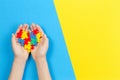 Child hand holding colorful heart on yellow and blue background. World autism awareness day concept