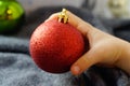 Kid hand holding red Christmas decoration shining balls, close up