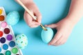 Kid hand painted Easter eggs, paints and brushes on a blue background. Preparation for the holiday. Girls hands draw a pattern