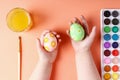 Kid hand painted Easter eggs, paints and brushes on a coral background. Preparation for the holiday. Girls hands draw a pattern