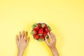 Kid hand taking strawberry from the bowl on yellow background