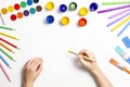 Kid hands painting at the table with art supplies, top view