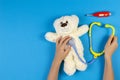 Kid hands with toy stethoscope, teddy bear and toy medicine tools on light blue background. Top view