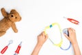 Kid hands with toy stethoscope, teddy bear and toy medicine tools on a white background. Top view.