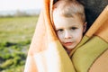 Kid hides in a blanket from the cold in a green meadow.