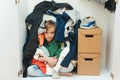 Kid hiding among messy clothes inside closet. Organization and storage of clothes at home