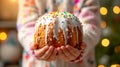 Kid holding in hands Easter cake Kulich decorated with white dripping icing and colored sprinkles. Blurred background