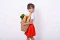 Kid holding paper grocery bag full of vegetables milk, bread. Happy child with grocery bag full of healthy food isolated on white.