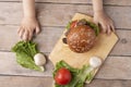 Kid holds mushroom burger above chopping board on wooden table