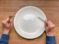 A kid is hungry. An empty white plate on a wooden table. Fork and knife. Fasting, dieting concept Royalty Free Stock Photo