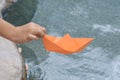 Kid launching small orange paper boat on water outdoors, closeup