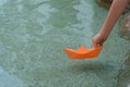 Kid launching small orange paper boat on water outdoors, closeup. Space for text