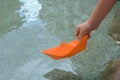 Kid launching small orange paper boat on water outdoors, closeup