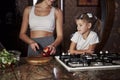 Kid learning how to cook. Pretty young woman standing in the modern kitchen near gas stove and teach daughter how to