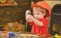 Kid learning to use screwdriver. Concentrated kid in orange helmet working in workshop. Future occupation concept Royalty Free Stock Photo