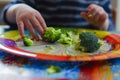 kid leaving behind uneaten broccoli on a colorful dinner plate