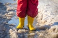 Kid legs in rainboots standing in the ice puddle