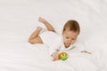 The kid lies in a snow-white bed, laughs and plays with a rattle. Royalty Free Stock Photo