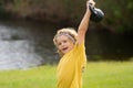 Kid lifting the kettlebell in park outside. Kid boy working out with dumbbells. Sport and kids training. Royalty Free Stock Photo