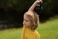 Kid lifting the kettlebell in park outside. Child boy raising a kettlebell. Cute child training with dumbbells. Kids Royalty Free Stock Photo