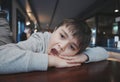 Kid looking out with bored face, Indoors Portrait preschool child laying head down on hand and yawning, Young boy sitting in