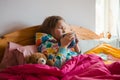 Kid lying in bed with pink blanket. Little girl with cold in scarf and blanket with hot beverage in hands near teddy Royalty Free Stock Photo