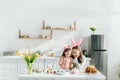 Kid and mother with bunny ears near chicken eggs, decorative rabbits, easter bread and tulips Royalty Free Stock Photo