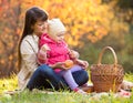 Kid and mother sit with apples basket outdoors in autumnal park